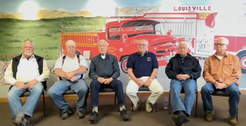 Six retired firemen sit in front of a Louisville Fire truck mural.