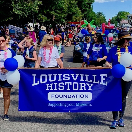 People marching in a parade holding a banner that reads, Louisville History Foundation, Supporting your museum