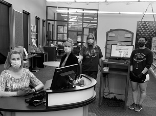 Four women wearing medical masks posed by a reference desk with computers.