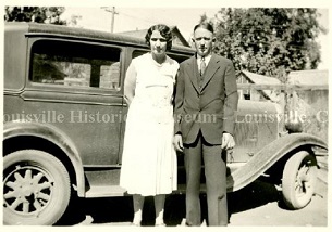 Historic photo of man and woman standing in front of an automobile.a