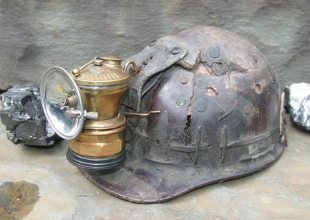 a cracked miners helmet with a bronze carbide lamp attached