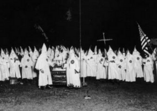 a group of people in KKK uniforms of white hoods with a cross and American flag