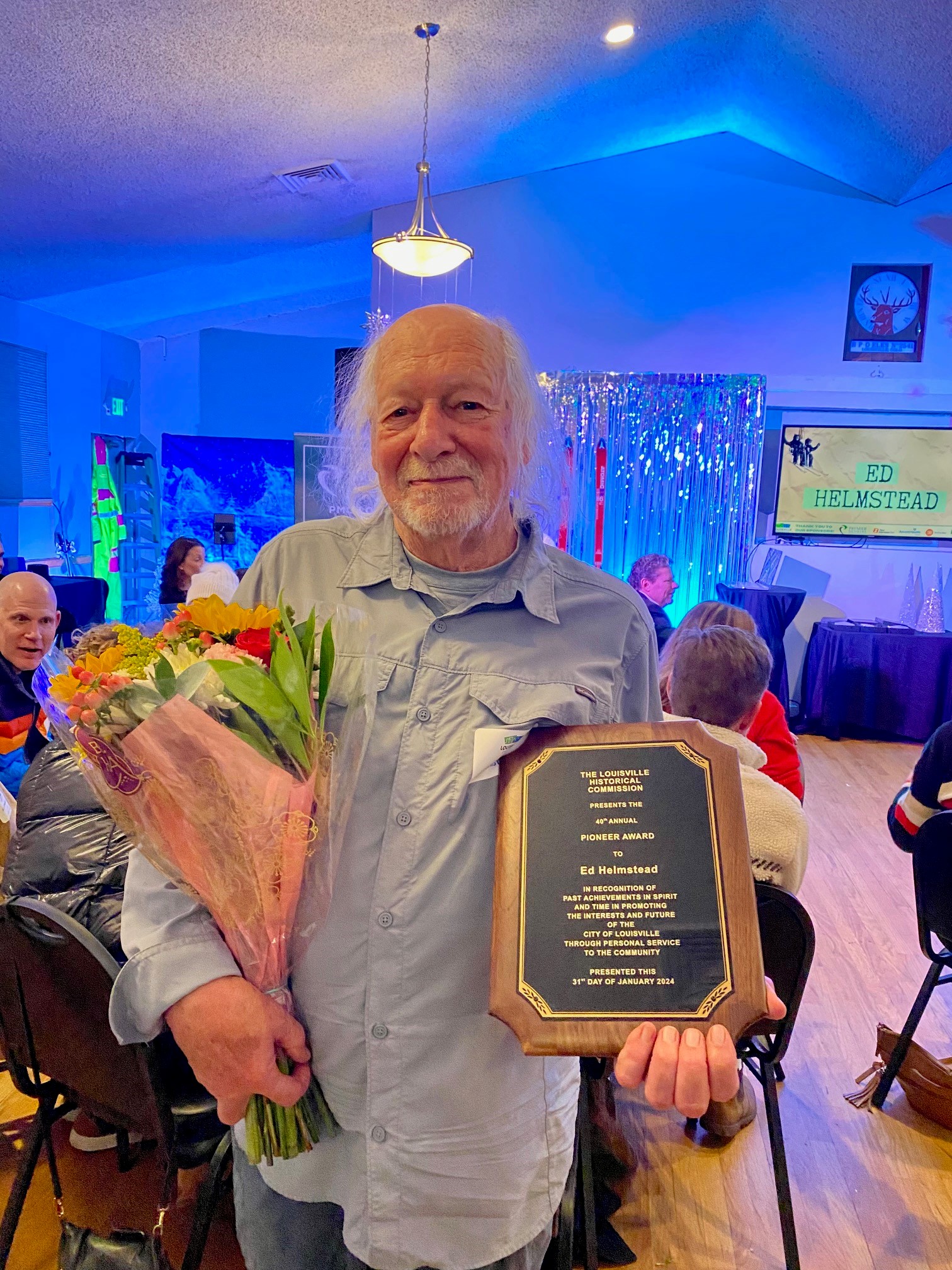 Ed Helmstead posing with flowers and the Pioneer Award plaque.