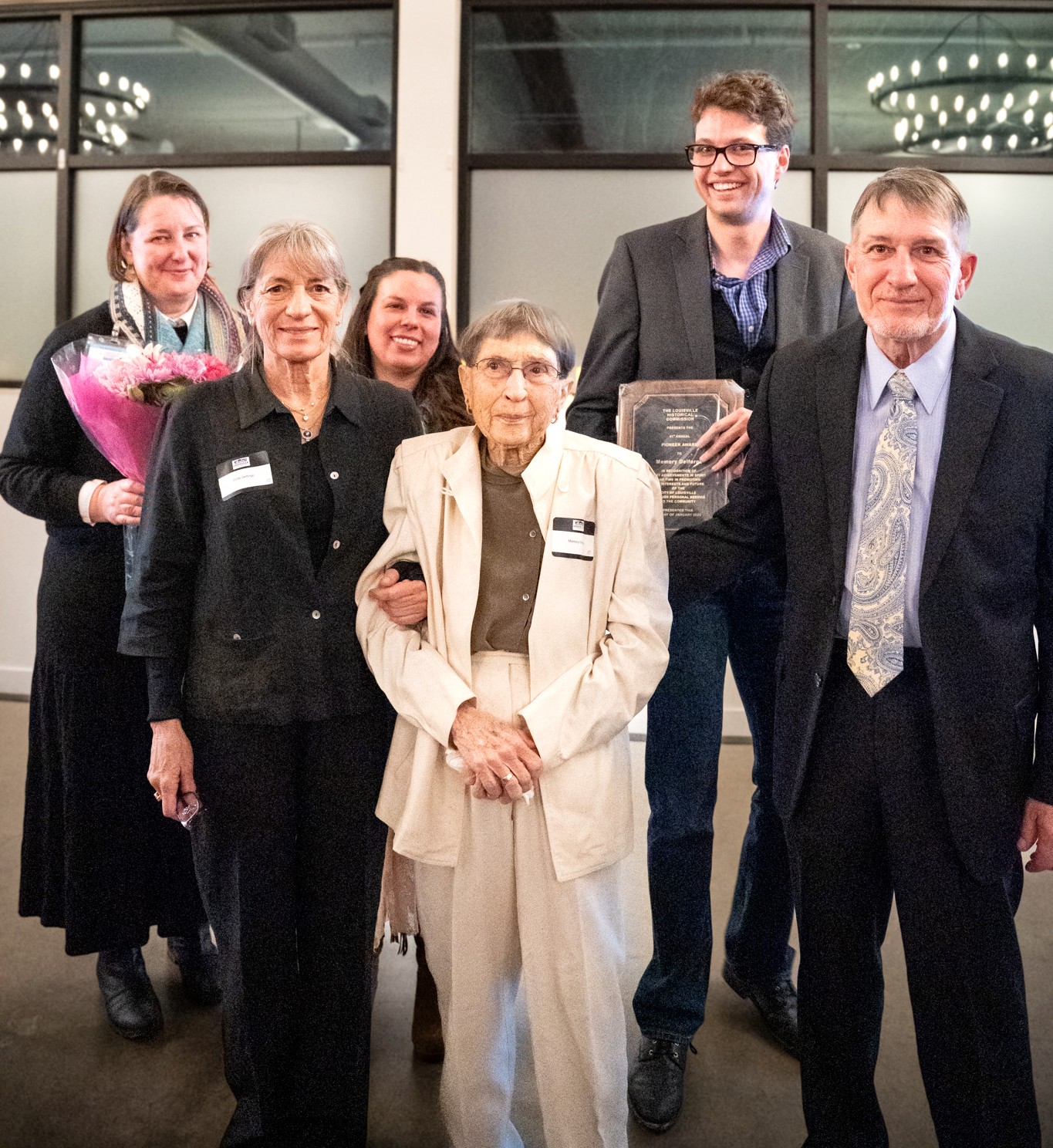 Memory Delforge in white, surrounded by her adult children and Historical Museum Advisory Board and History Foundation members holding plaque and flowers