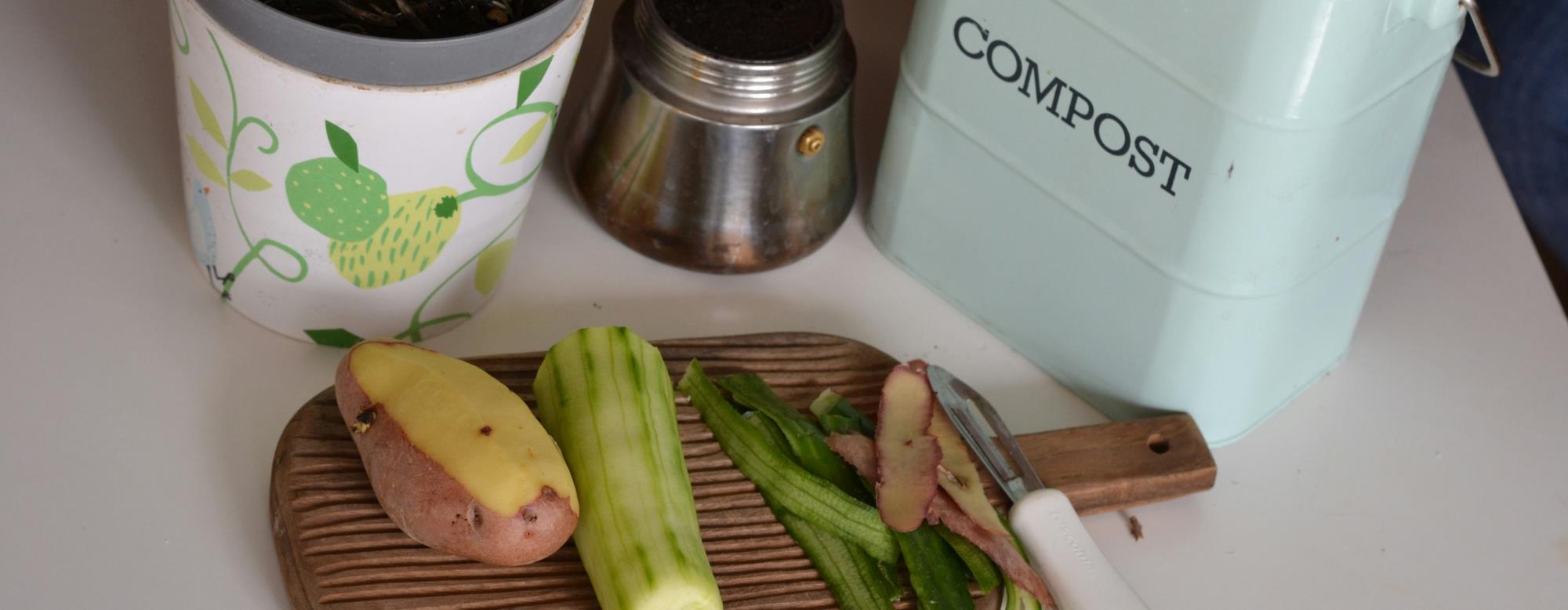 Vegetables on a cutting board sitting next to a compost bucket.