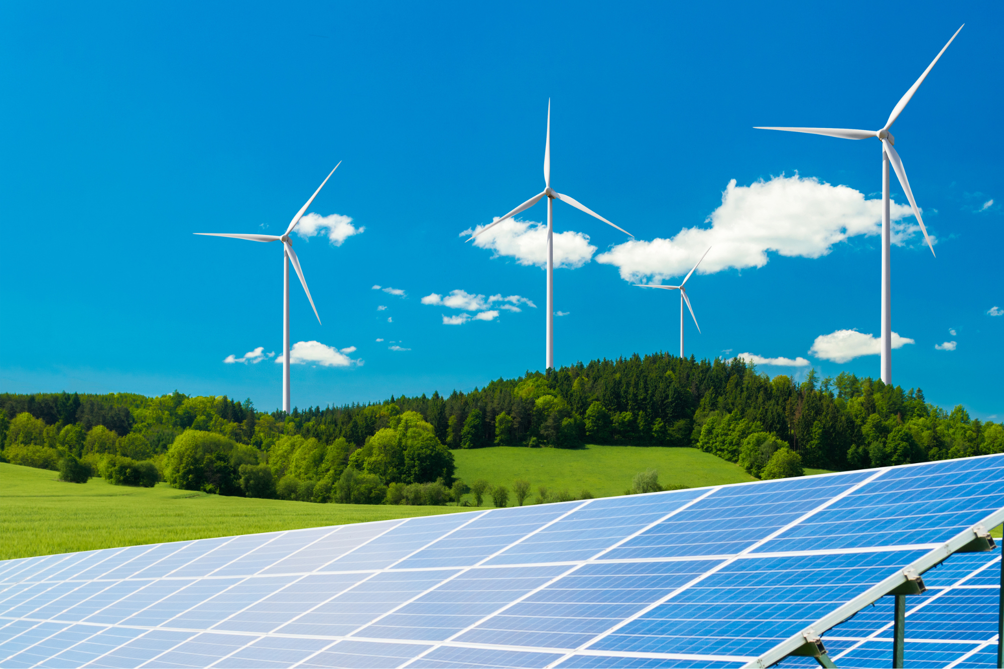 Photo of a solar field with a green hill and windmills in the background