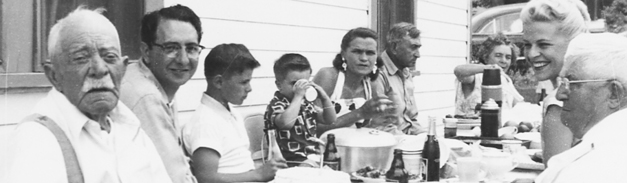 black and white photo of multi-generational group around a dinner table eating and smiling